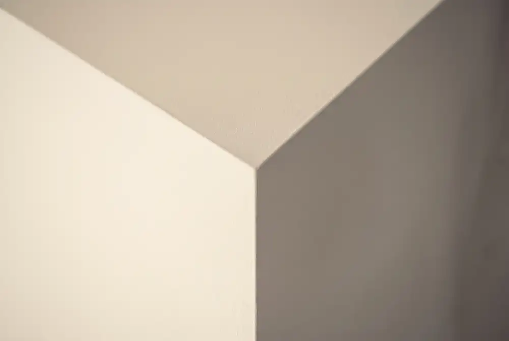 Extreme close-up of a freshly stopped and painted square-set internal corner, a sharp ninety-degree arris under raking light.